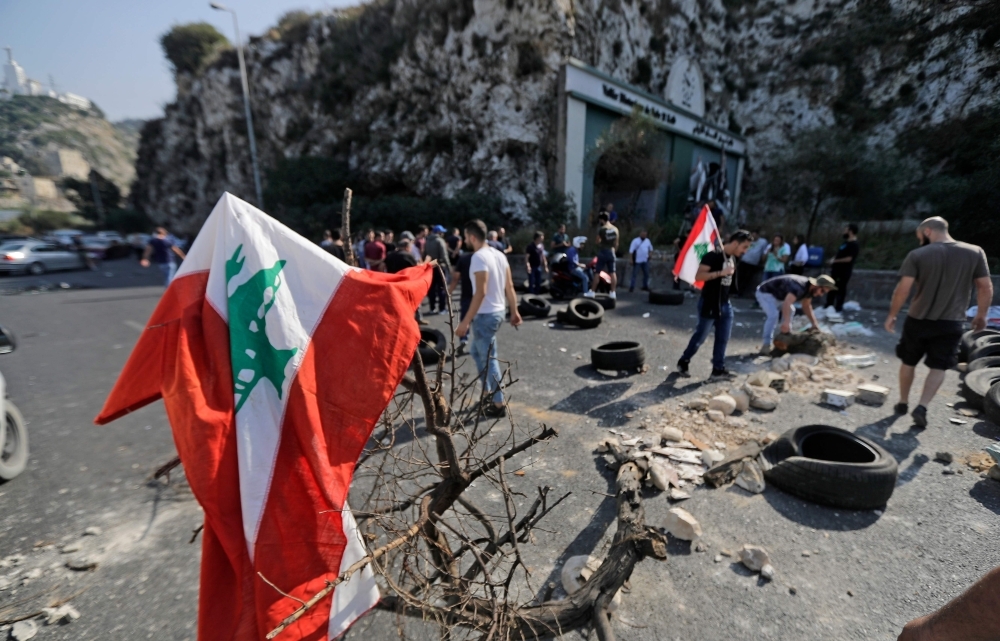 A Lebanese youth waves a national flag in front of burning tires blocking the Beirut-Tripoli highway in the coastal town of Ghazir, north of the port city of Junieh, during continuing anti-government protests across Lebanon on Wednesday. -AFP