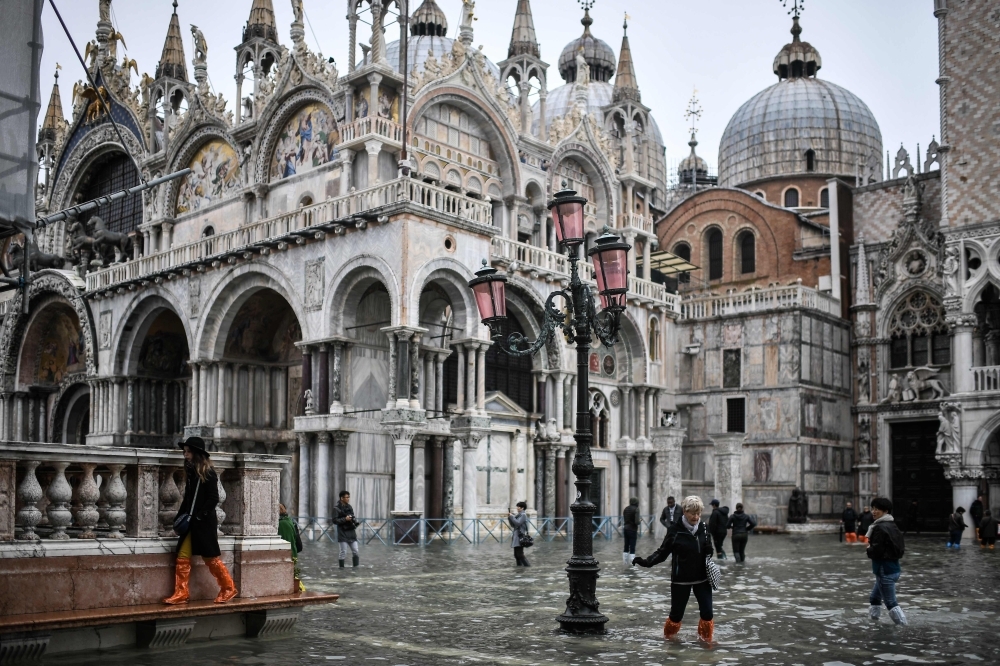 Pedestrians walk on a footbridge across the flooded Riva degli Schiavoni embankment after an exceptional overnight 