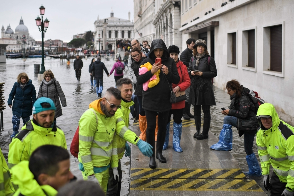 Pedestrians walk on a footbridge across the flooded Riva degli Schiavoni embankment after an exceptional overnight 