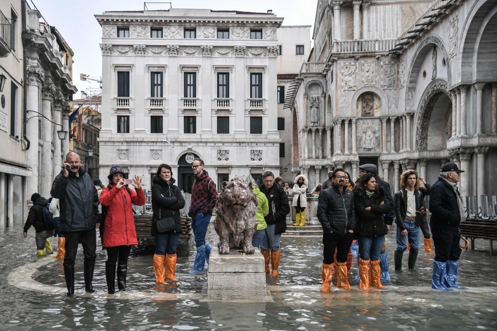 Pedestrians walk on a footbridge across the flooded Riva degli Schiavoni embankment after an exceptional overnight 