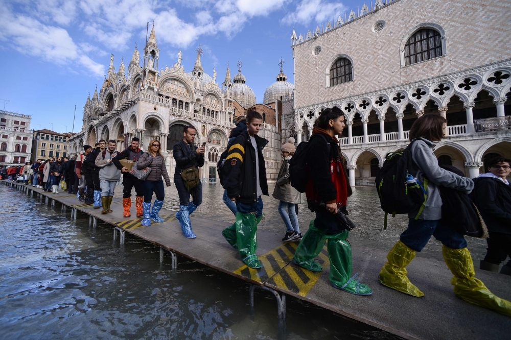 People walk on a footbridge across the flooded St. Mark's Square by St. Mark's Basilica, rear, and the Doge's palace, right, in Venice, Italy, on Thursday. — AFP