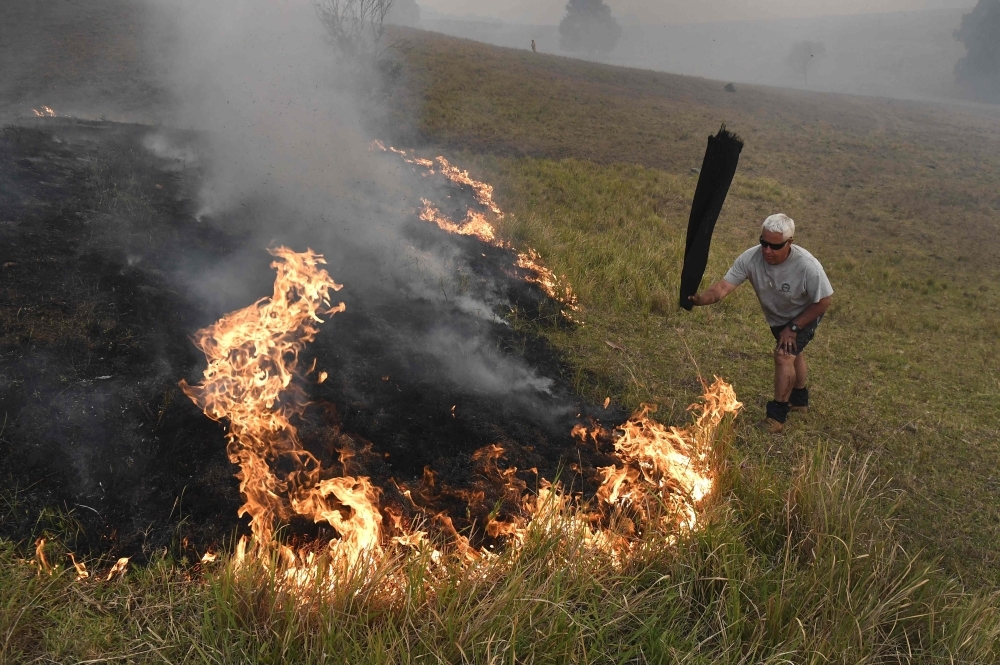 A man uses a wet towel to help put out flames as they encroach on farmland near the town of Taree, some 350 km north of Sydney, on Thursday. — AFP