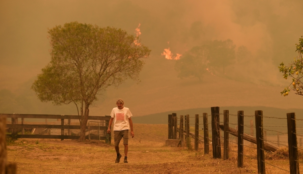 A man uses a wet towel to help put out flames as they encroach on farmland near the town of Taree, some 350 km north of Sydney, on Thursday. — AFP