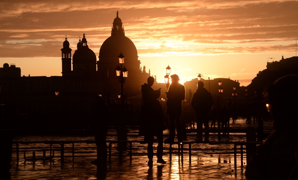 Visitors walk at the sunset in the flooded street in Venice, during 