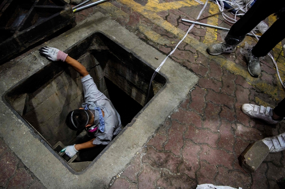 A protester climbs down into a sewer entrance with a guide string, center, as he and others try to find an escape route from the Hong Kong Polytechnic University in the Hung Hom district of Hong Kong, early morning on Tuesday. — AFP