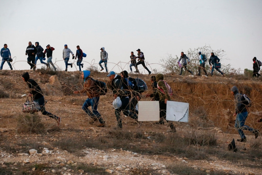 Palestinian labourers wait to cross illegally into Israeli areas through a hole in Israel's illegal barrier wall on November 20, 2019, in the southern Israeli city of Beer Sheva. -AFP