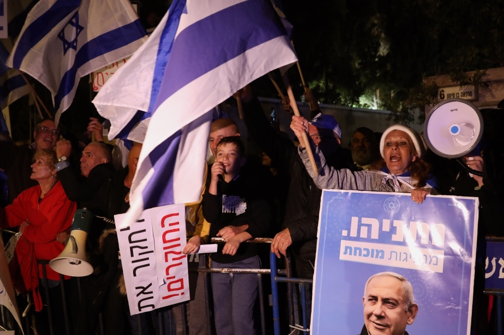 Supporters of Israeli Prime Minister Benjamin Netanyahu wave flags and placards as they rally to express their solidarity, outside his Jerusalem office on Saturday. -AFP