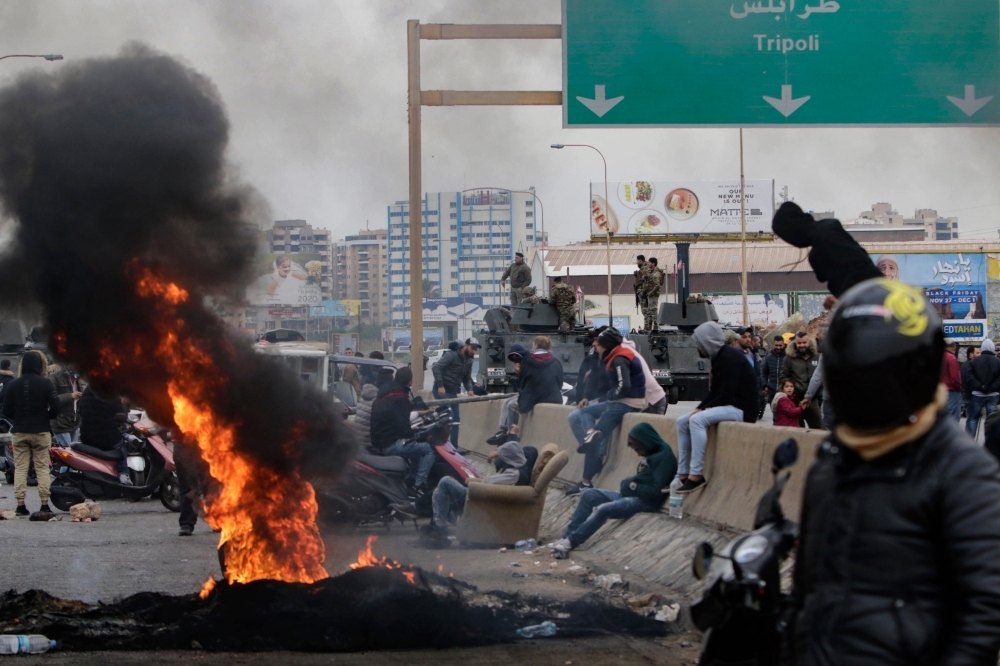 Lebanese anti-government protesters burn tires to block the road leading to the southern entrance of the northern port city of Tripoli on Monday. — AFP