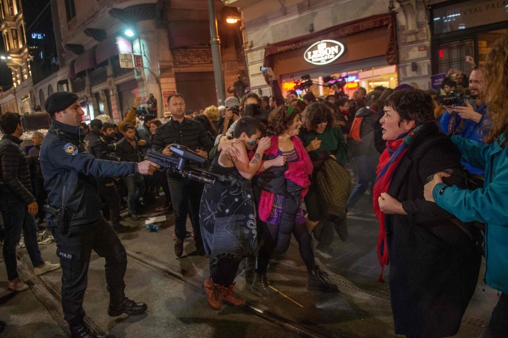 A Turkish riot police officer uses a non-lethal hand-held weapon during clashes with women's rights activists as they take part in a march towards Taksim Square in Istanbul on Monday. -AFP