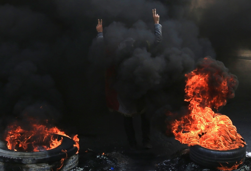 An Iraqi demonstrator gestures as he stands next to burning tires in the city of Karbala, south of Iraq's capital Baghdad, on Tuesday. — AFP