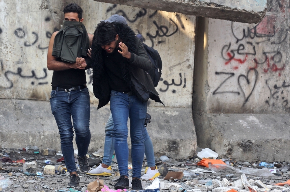 Iraqi youths duck as they run off amid clashes between anti-government demonstrators and security forces in the capital Baghdad's Al-Rasheed street near Al-Ahrar bridge on Tuesday. — AFP