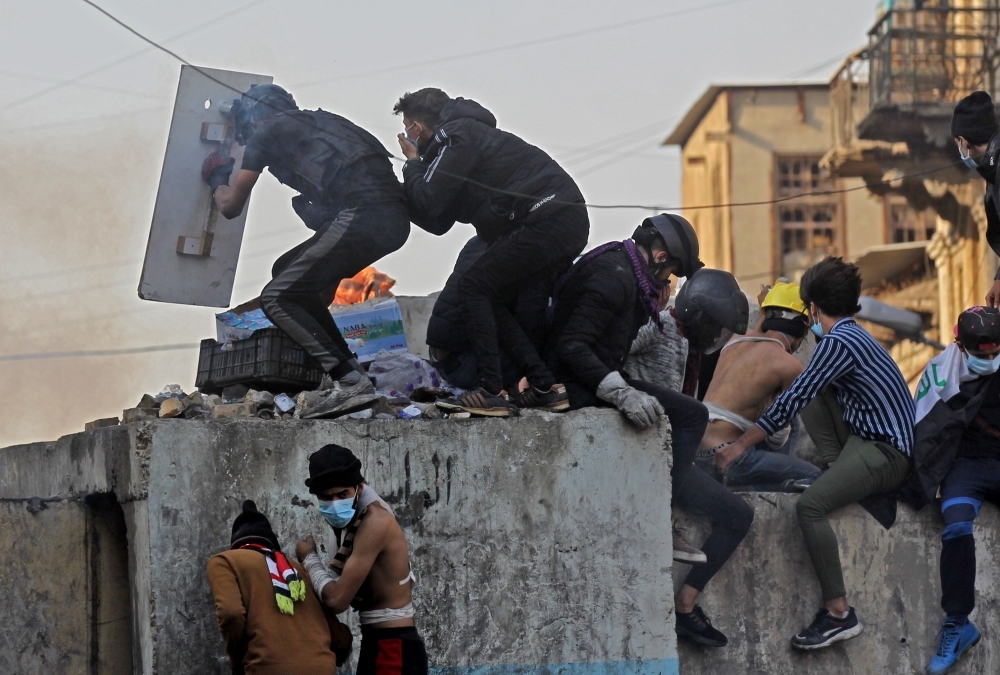 Iraqi youths duck as they run off amid clashes between anti-government demonstrators and security forces in the capital Baghdad's Al-Rasheed street near Al-Ahrar bridge on Tuesday. — AFP