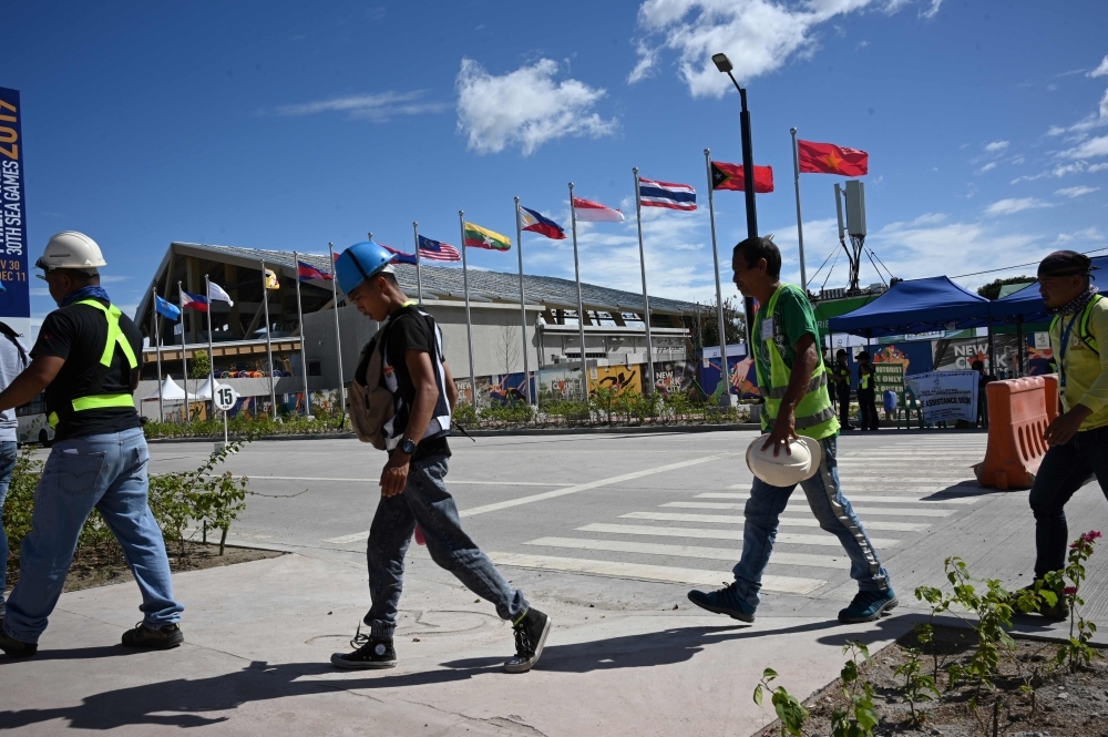 Workers walk past ASEAN members' flags next to the Aquatic centre in New Clark City, in Capas town, Tarlac province north of Manila, days ahead of the opening ceremony of SEA Games (Southeast Asian Games). — AFP 