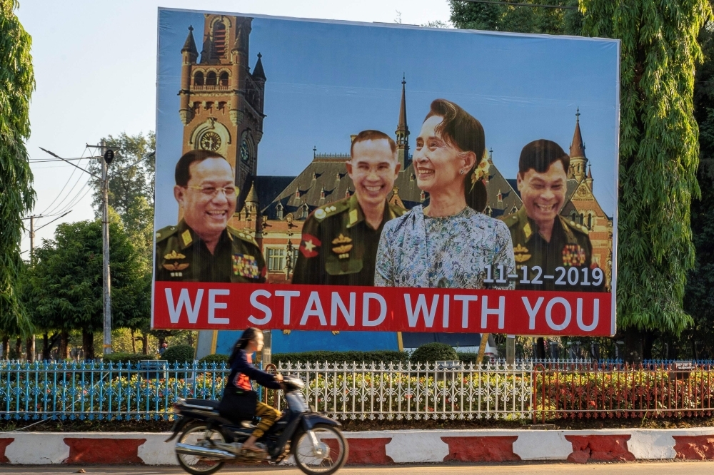 A woman on motorcycle rides past a huge billboard depicting Myanmar State Counselor Aung San Su Kyi with the three military ministers, from left, Border Affairs Minister Lt. Gen. Ye Aung, Defense Minister Lt. Gen. Sein Win and Home Affairs Minister Lt. Gen. Kyaw Swe with the background, showing the building of the International Court of Justice in The Hague, displayed along a main road in Hpa-an, Karen State, on Thursday. — AFP