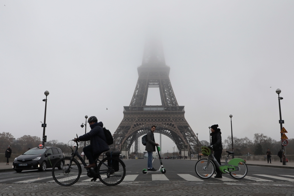 People ride bicycles and electric scooter past the Eiffel tower partially hidden by fog in Paris on Thursday. — AFP