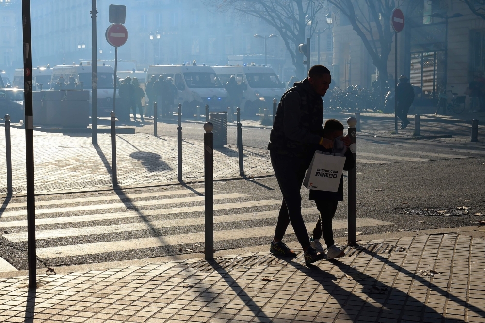 A man and his child walk to avoid tear gas smoke on the sidelines of a demonstration against the pension overhauls, in Bordeaux, France, on Thursday. — AFP