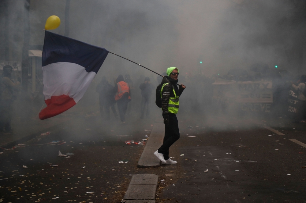 A man and his child walk to avoid tear gas smoke on the sidelines of a demonstration against the pension overhauls, in Bordeaux, France, on Thursday. — AFP