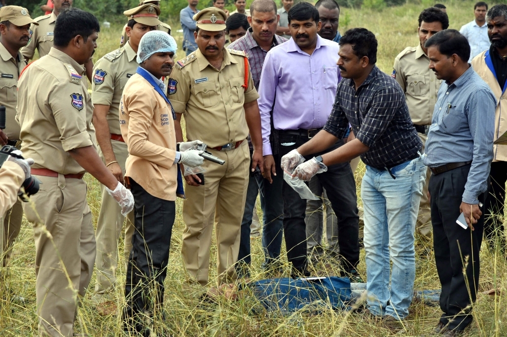 A forensic official, third left, holds a gun as police officers gather around the body of man at the site where Police officers shot dead four detained gang rape and murder suspects in Shadnagar, some 55 km from Hyderabad, on Friday. — AFP