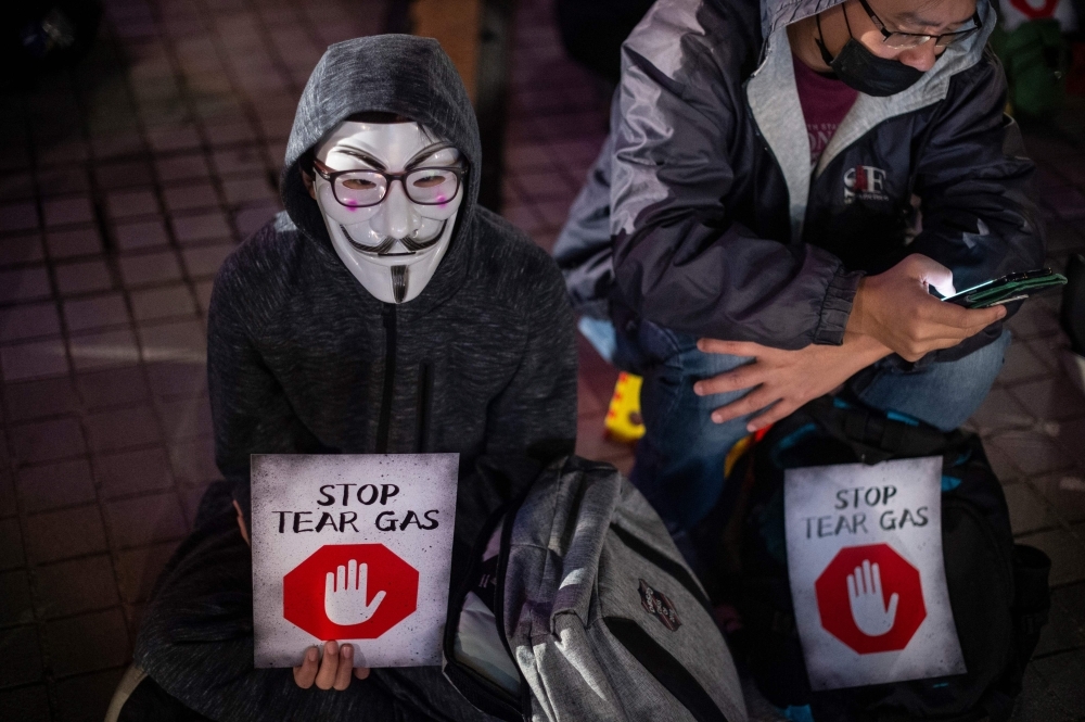 A participant wearing a Guy Fawkes mask holds a placard during a 