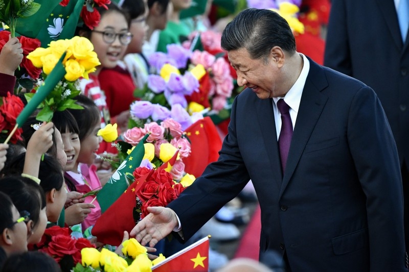 China's President Xi Jinping greets children waving the flags of China and Macau upon his arrival at Macau's international airport in Macau on Wednesday. -AFP