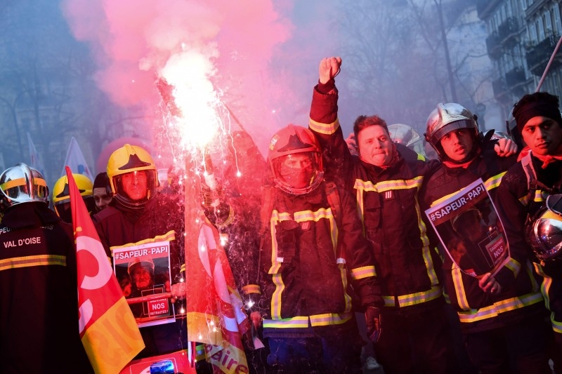  Men dressed firefighters uniforms wave flags of the French trade union General Confederation of Labor (Confederation Generale du Travail - CGT) and burn flares as they take part in a demonstration in Paris on Tuesday to protest against the French government's plan to overhaul the country's retirement system, as part of a national general strike. -AFP