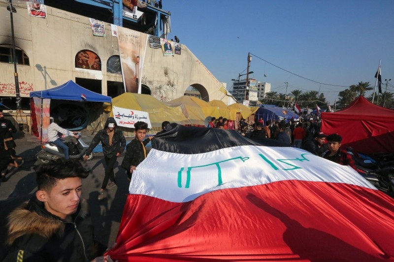Iraqi anti-government protesters carry a large national flag during ongoing demonstrations in the capital Baghdad's Tahrir square, on Sunday. -AFP