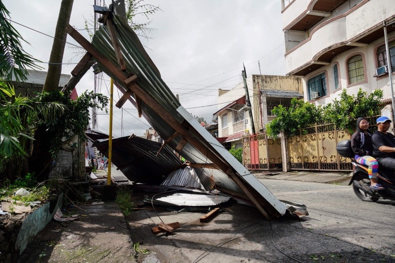 A motorist commutes past a blown down galvanised roof from a house damaged during the height of Typhoon Phanfone in Tacloban, Leyte province in the central Philippines on Wednesday. -AFP
