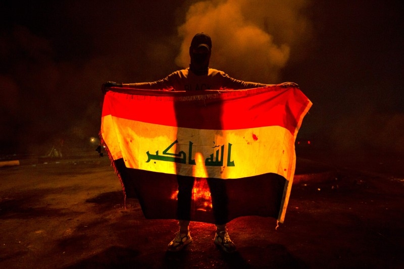 An Iraqi anti-government protester stands holding up a national flag at a make-shift roadblock in the southern city of Basra late on Tuesday. -AFP