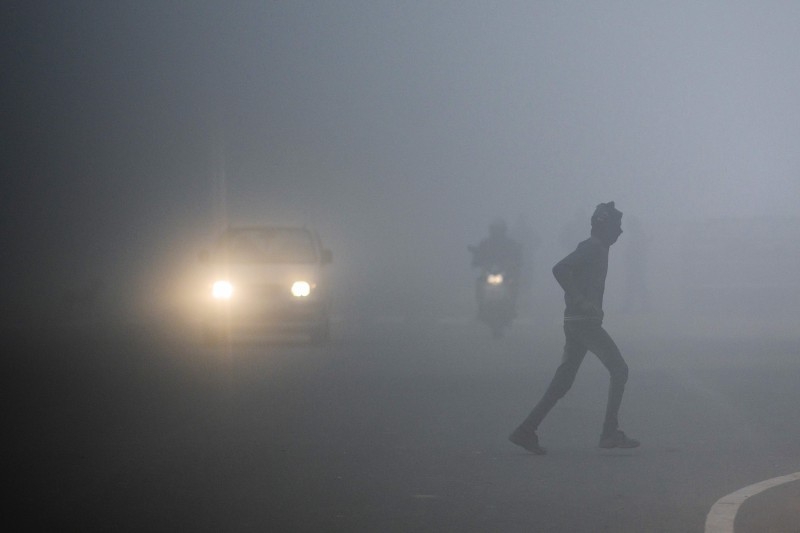 A man crosses a street as commuters make their way under heavy foggy conditions in New Delhi on Monday. -AFP