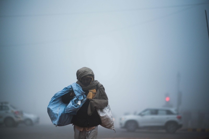 A man crosses a street as commuters make their way under heavy foggy conditions in New Delhi on Monday. -AFP