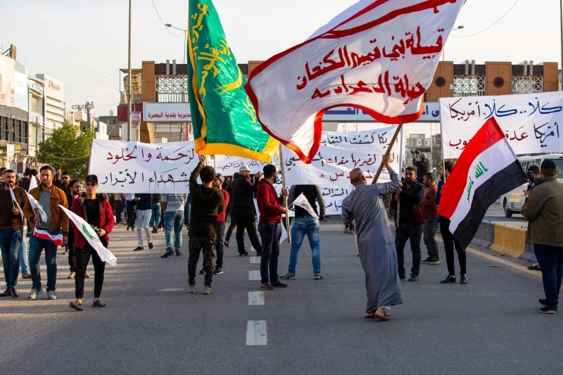 Iraqis wave Hashed Al-shaabi armed network flags in the southern city of Basra on Monday, during a demonstration to denounce the previous night's attacks by US planes on several bases belonging to the Hezbollah brigades near Al-Qaim, an Iraqi district bordering Syria.   -AFP