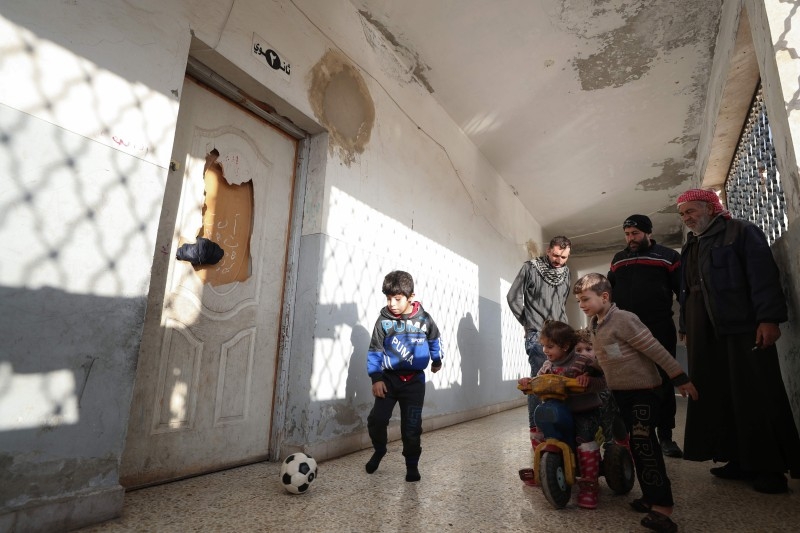 Abdul Razzak, right, a 65-year-old Syrian man displaced with his family from Maaret Al-Numan, watches his grandchildren play in a hallway of a school turned into a makeshift shelter in Ariha town, in the south of Syria's northwestern province of Idlib, on Tuesday. — AFP