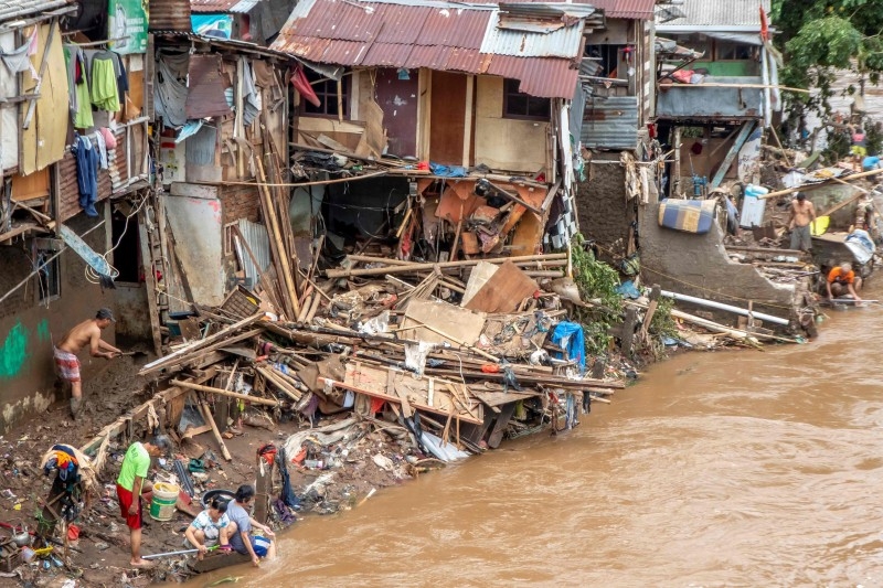Indonesians clean their homes and cutlery along the river in Jakarta on Friday, after flooding triggered by heavy rain which started on New Year's Eve hit the area. Indonesian rescuers mounted a desperate search for those missing after flash floods and landslides sparked by torrential rains killed at least 43 people across the Jakarta region, leaving whole districts under water and thousands homeless. — AFP