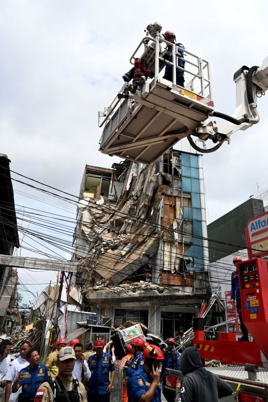 Rescuers search a five-story building (behind) after part of the structure collapsed in Jakarta on Monday. -AFP