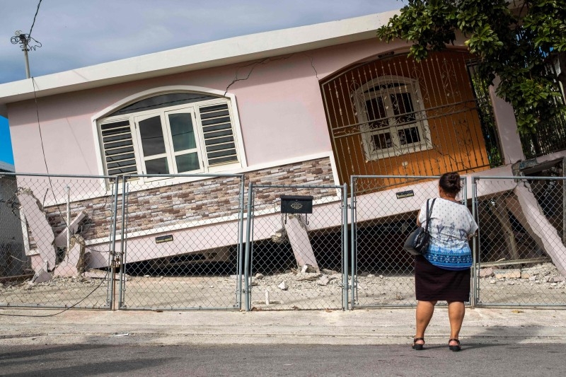 A woman stands in front of a house damaged by a 5.8 earthquake in Guanica, Puerto Rico, on Monday. — AFP