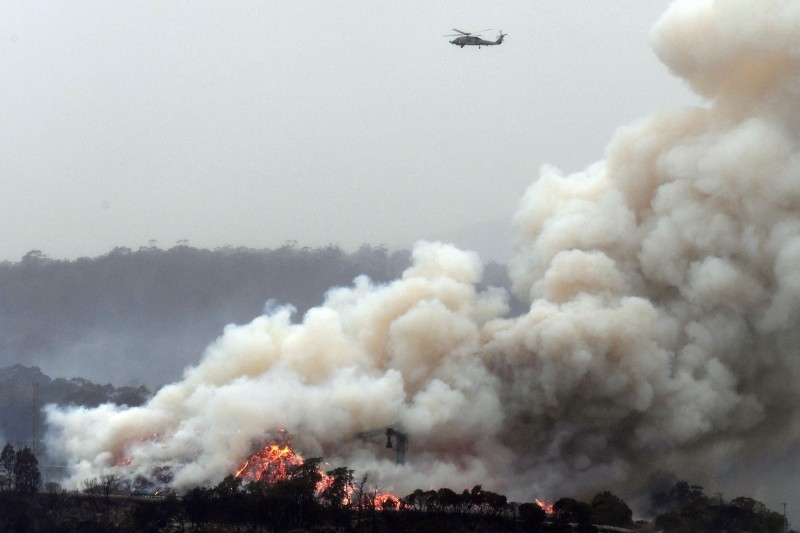 A military helicopter flies above a burning woodchip mill in Eden, in Australia's New South Wales state. — AFP