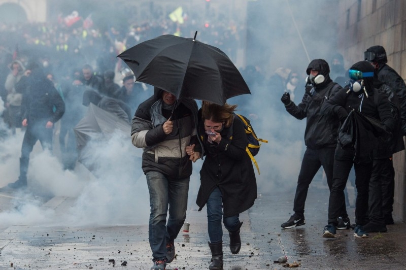 People run for cover during a protest called by the 'Yellow Vest' (gilets jaunes) anti-government movement as part of a nationwide multi-sector strike against the French government's pensions overhaul, in Nantes, western France, on Saturday. — AFP