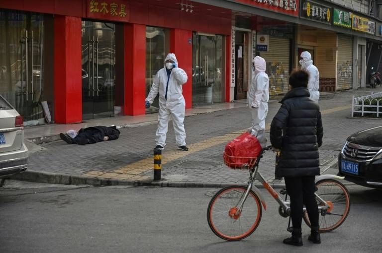 Officials in protective suits stand near an elderly man wearing a mask who collapsed and died on a street near a hospital in Wuhan. — AFP