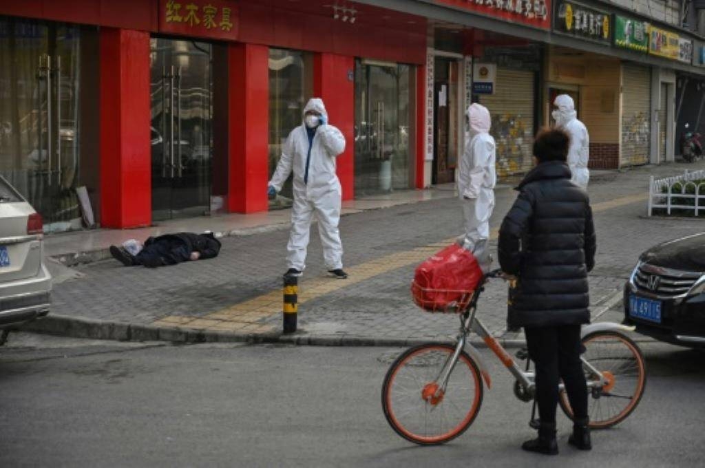 Officials in protective suits stand near an elderly man wearing a mask who collapsed and died on a street near a hospital in Wuhan, China. — AFP