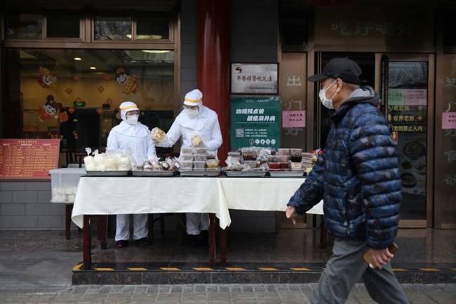 Restaurant workers wear protective clothing as they prepare food to sell on the street outside their restaurant in Beijing. — AFP 