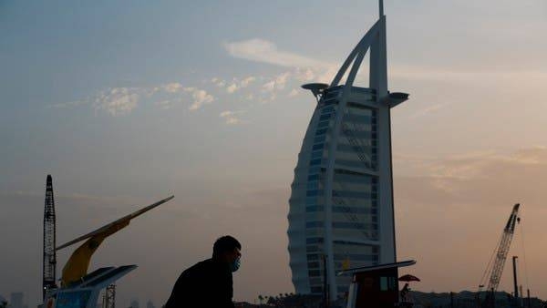 A tourist wearing a surgical mask bends down to take a picture in front of the sail-shaped Burj Al Arab luxury hotel in Dubai. -- Courtesy photo