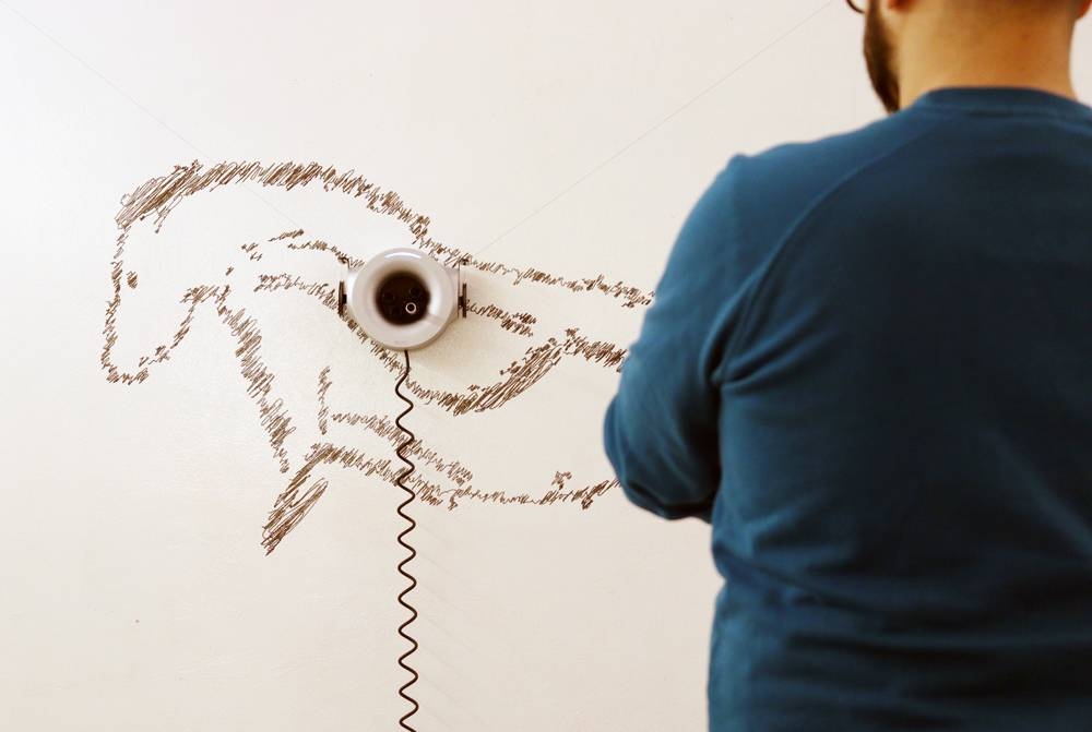 Scribit drawing on the wall with a person focusing on his effort.