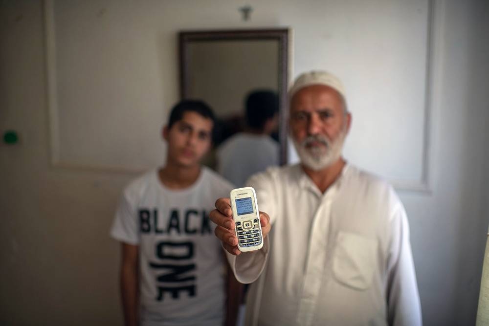 Yemeni refugee, Ibrahim, holds up his phone with his 15-year-old son Ishaak in Amman. 