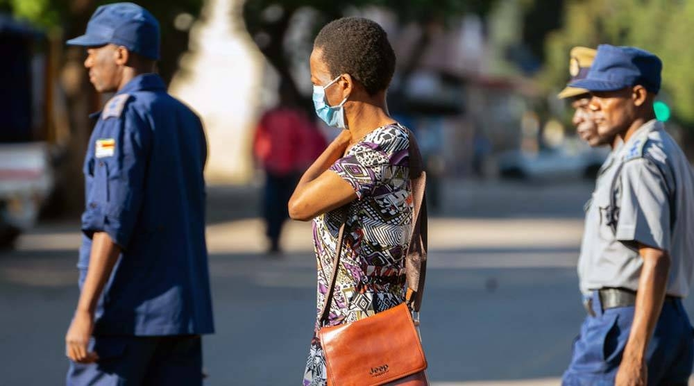 A woman wearing a COVID-19 protective mask walks past a group of police officers on patrol in Harare, Zimbabwe. — courtesy ILO/KB Mpofu