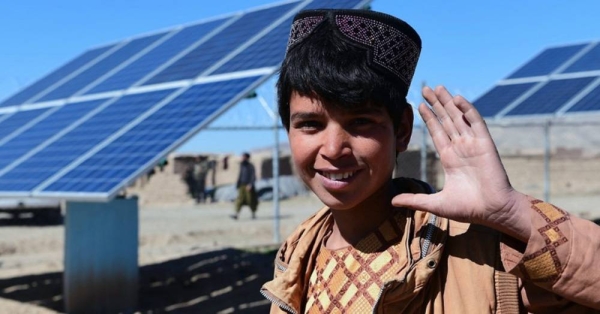 A boy waves in front of solar panels that provide electricity to pump water, in Herat, western Afghanistan. — courtesy UNICEF/Frank Dejongh