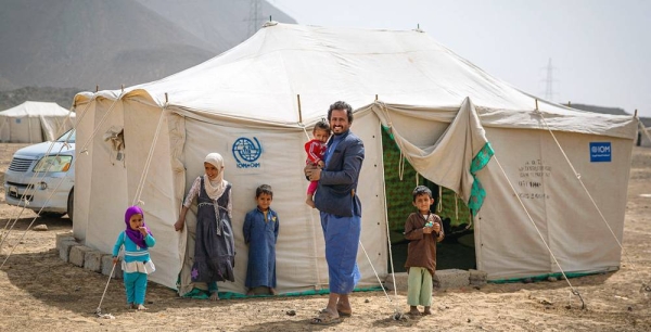 File photo shows a father standing with his children outside their tent in a displacement site outside Marib City, Yemen. — courtesy IOM/Olivia Headon