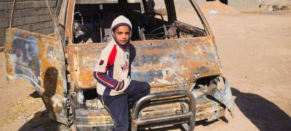 A young boy in Iraq stands next to a car that was torched by Daesh in this courtesy file photo.