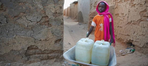 A nine-year-old girl pushes a wheelbarrow loaded with water-filled jerrycans in a IDP camp in Darfur, Sudan, in this courtesy file photo.
