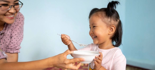 A mother helps her three-year-old girl eat porridge at home in Kyrgyzstan.