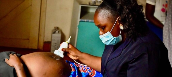 A midwife examines a pregnant woman using a portable ultrasound device.